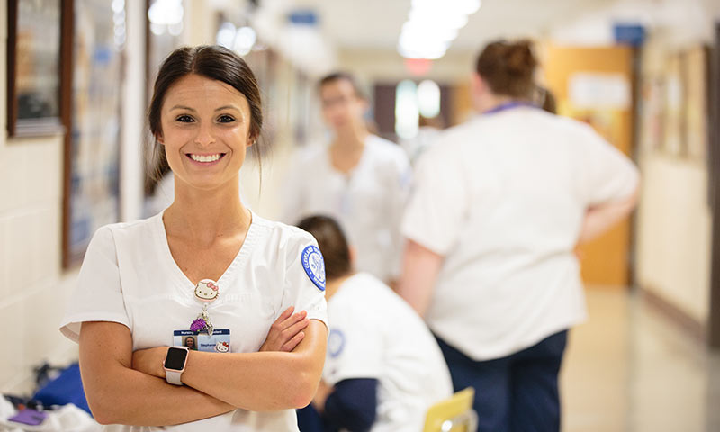 A nursing student in scrubs smiling with other students in the background